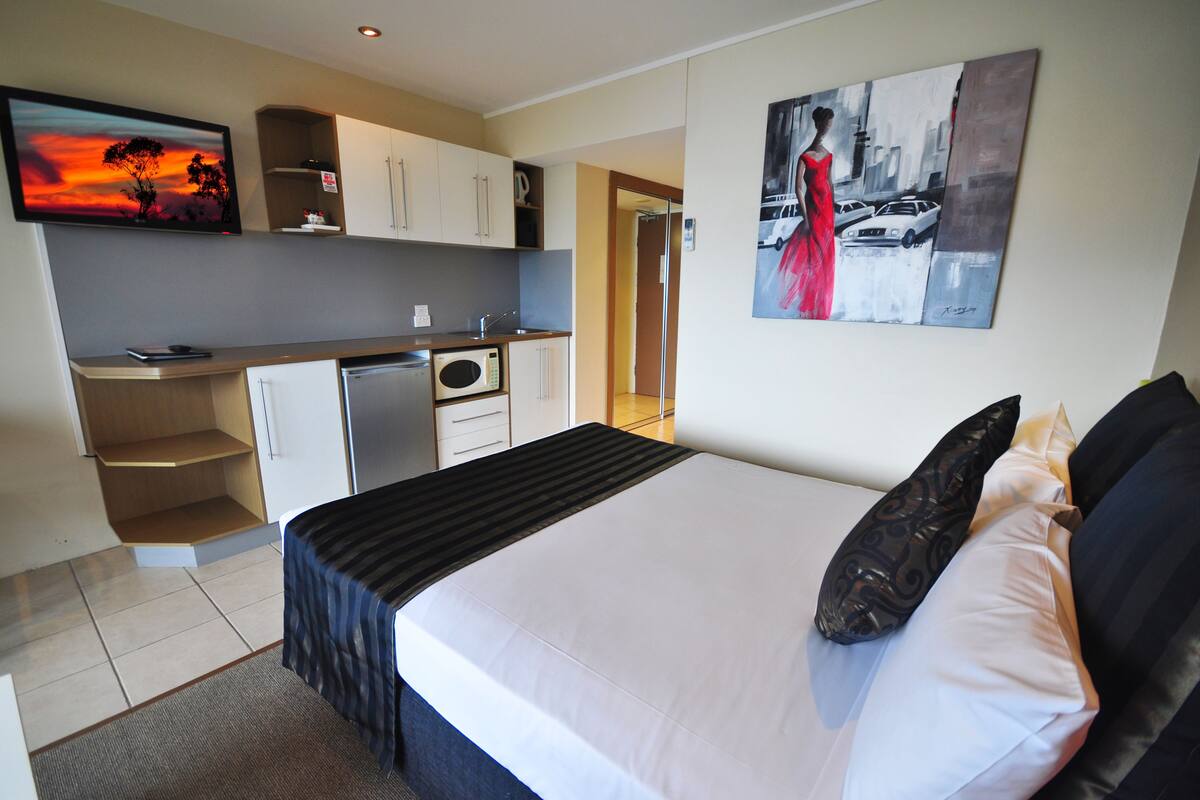 Una habitación de hotel con una cama, un escritorio, un microondas y un cuadro en la pared.