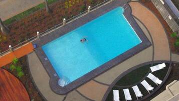 A rectangular swimming pool with a tiled deck surrounding it, a circular seating area with white loungers, and a small circular hot tub.