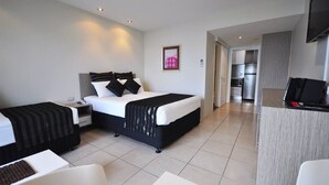 Una habitación de hotel con cama, mesitas de noche, escritorio y kitchenette.
