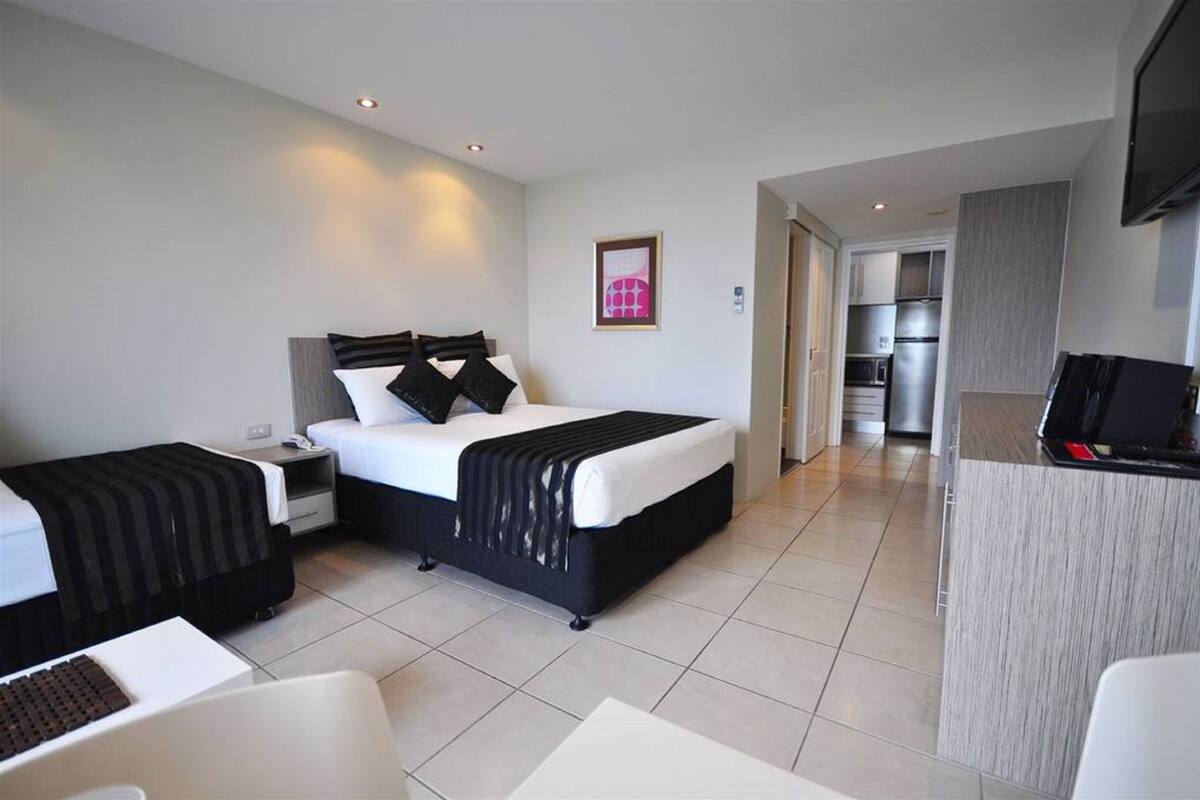 Una habitación de hotel con cama, mesitas de noche, escritorio y kitchenette.