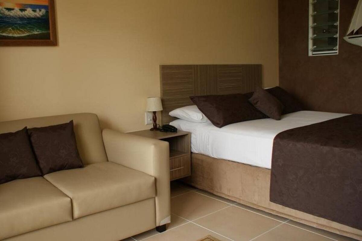 Habitación de hotel con cama, sofá, mesita de noche y un cuadro en la pared.