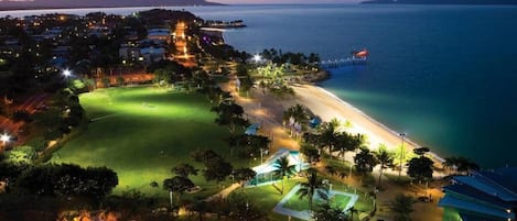 An aerial view of a coastal resort with a beachfront, a well-lit golf course, and a marina.