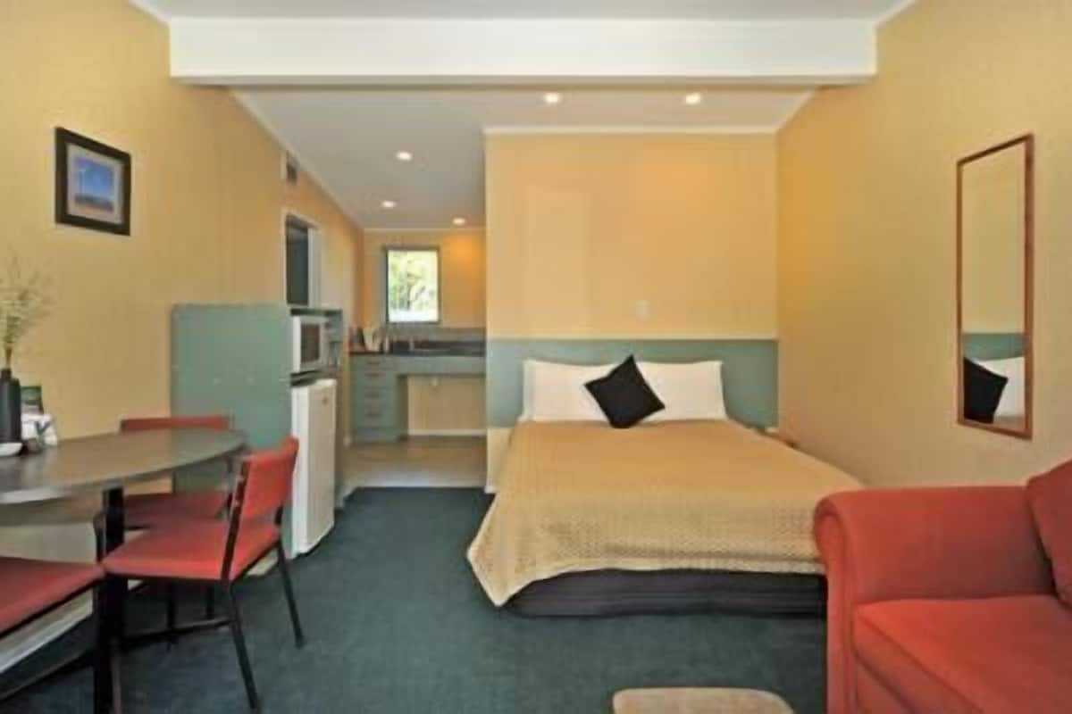 A compact hotel room with a bed, a sofa, a dining table, and a kitchenette.