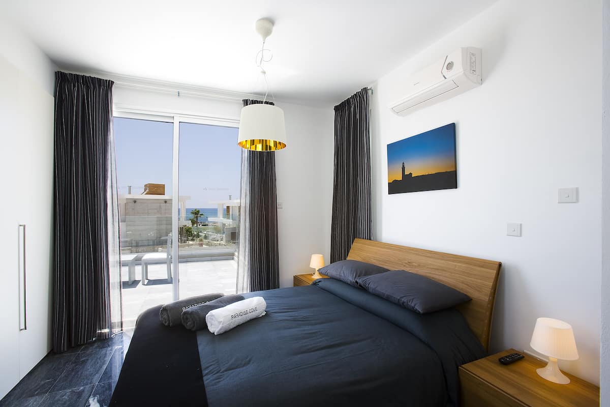Moderni hotellihuone, jossa on suuri sänky, yöpöytä, lamppu, taulu ja näkymä ulos.