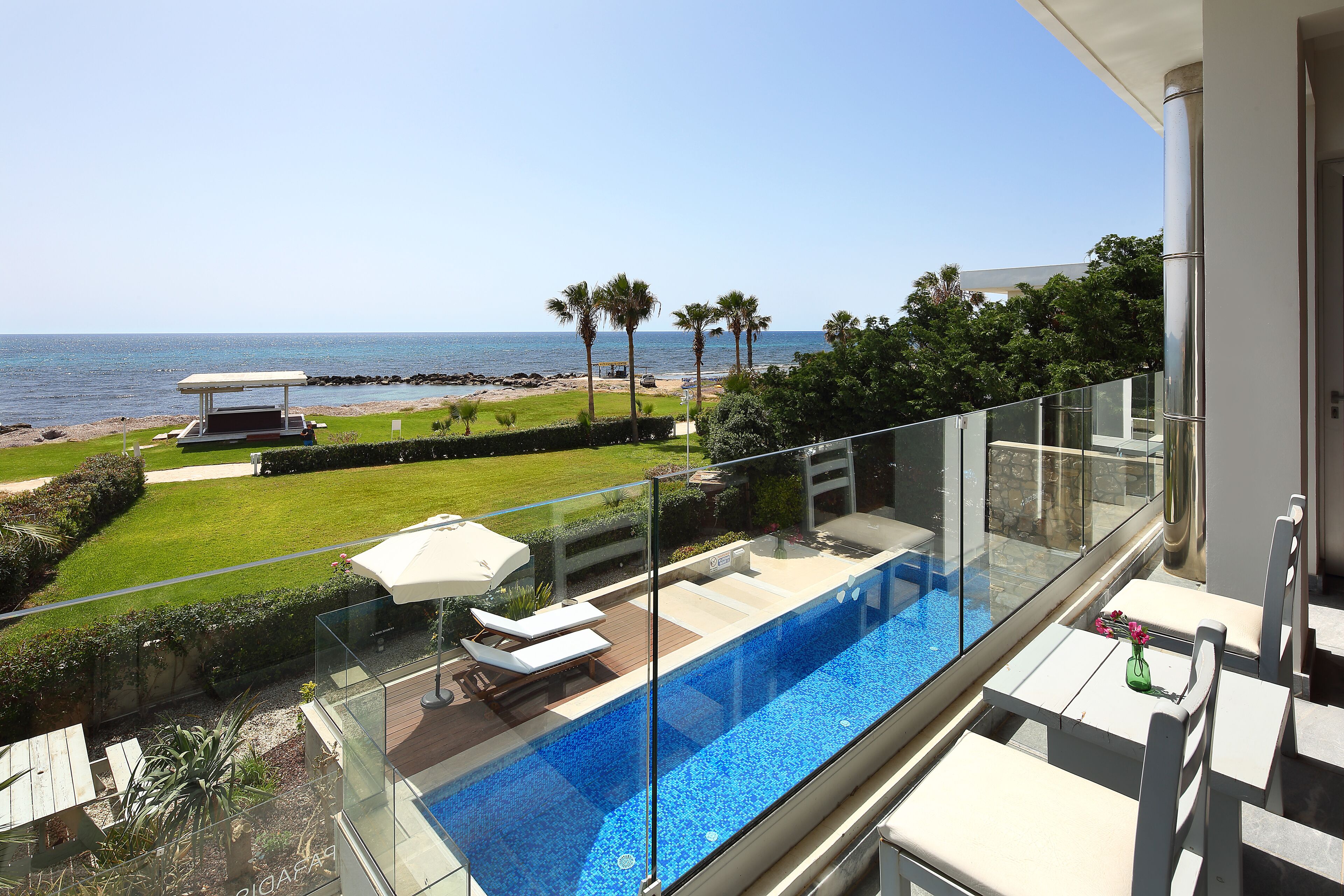 A balcony with a glass barrier overlooking a pool and a view of the sea.