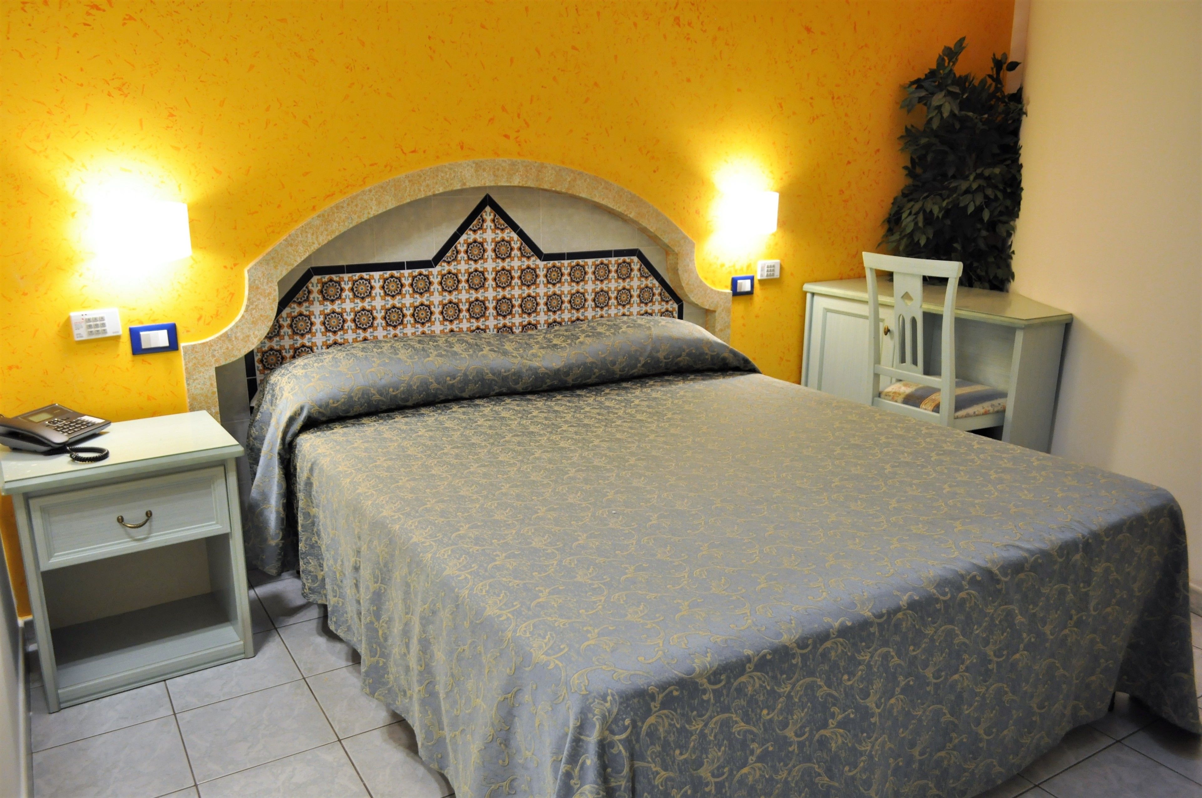 A bed with a patterned headboard, two bedside tables, a nightstand, and a small cabinet.