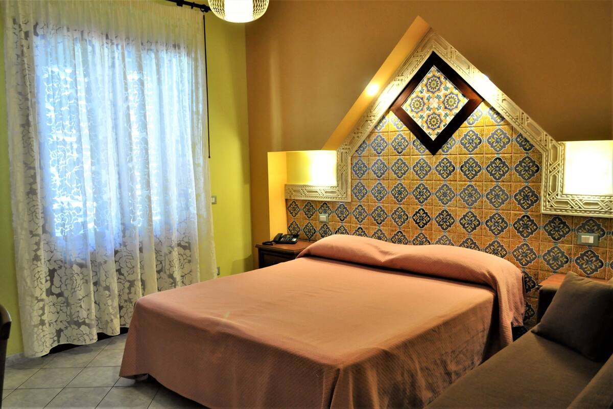 A hotel room with a bed, two bedside tables, a nightstand, and a decorative wall with patterned tiles.