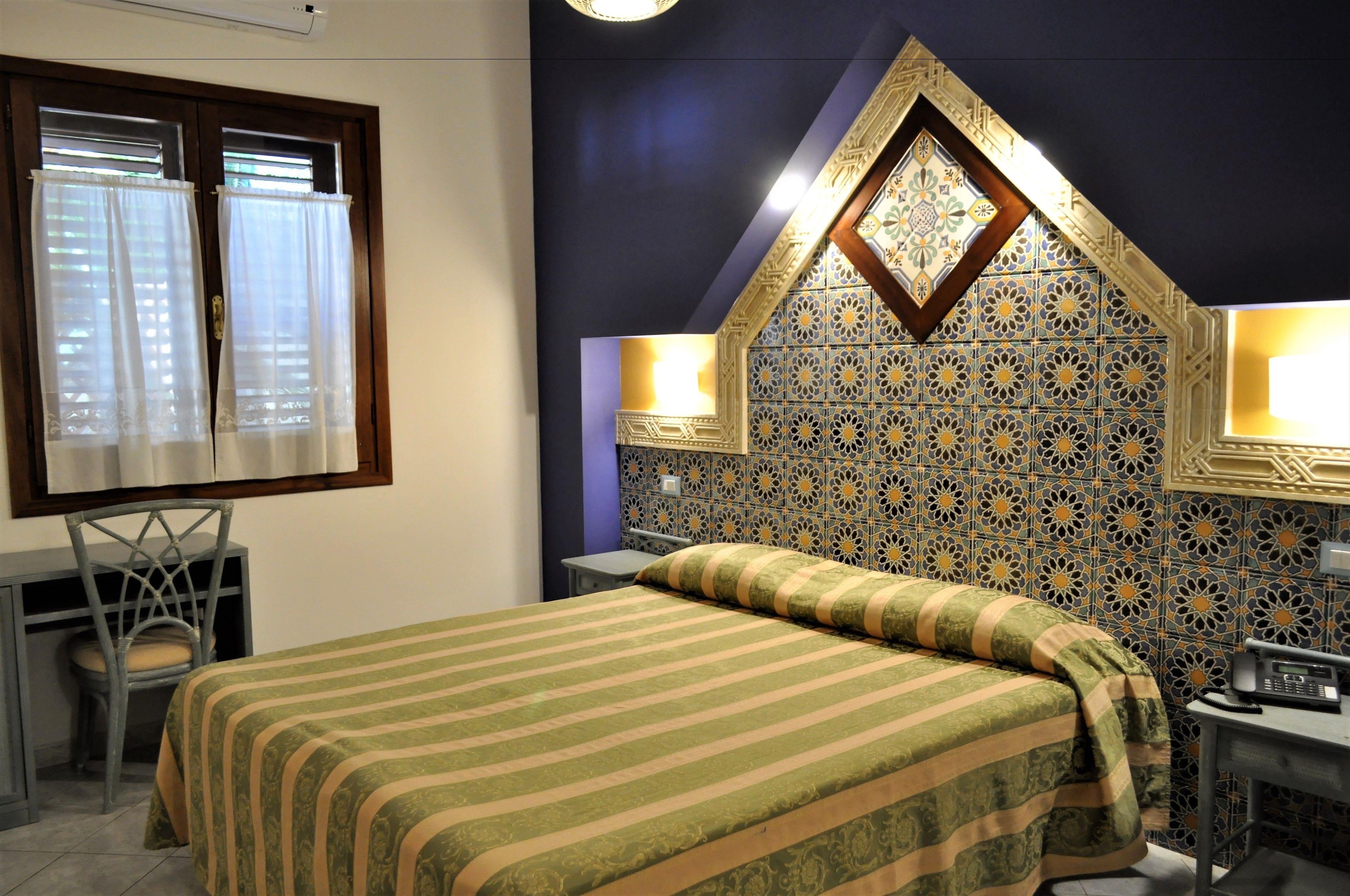 A room with a bed, a desk, a chair, and a decorative wall.