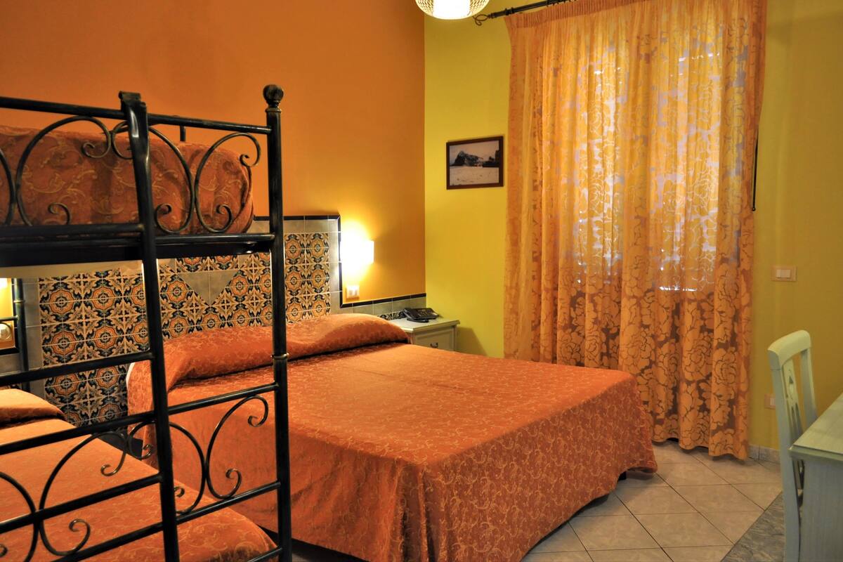 A room with a bed, a nightstand, a lamp, a chair, and a window with curtains.