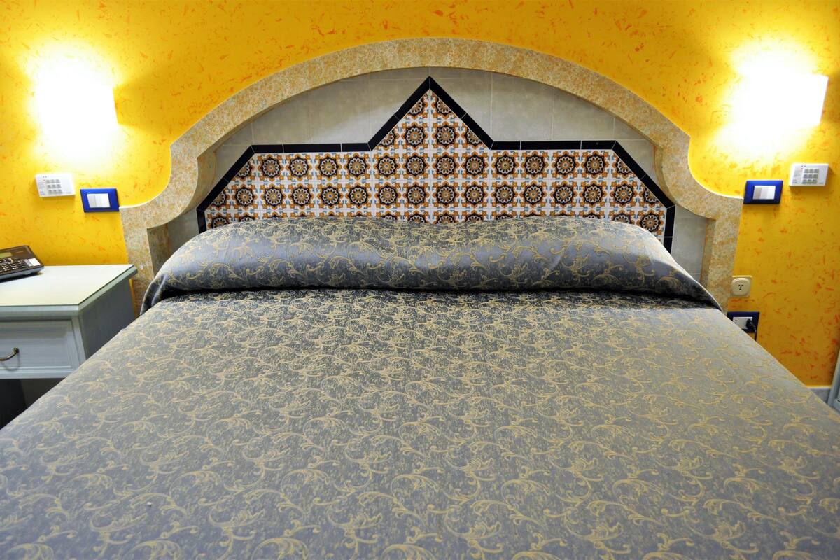 A bed with a patterned headboard and a nightstand with a lamp.