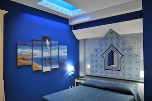 A room with a blue wall, a bed, a skylight, and a decorative wall tile. - Hotel Al-Taïr (San Vito Lo Capo)