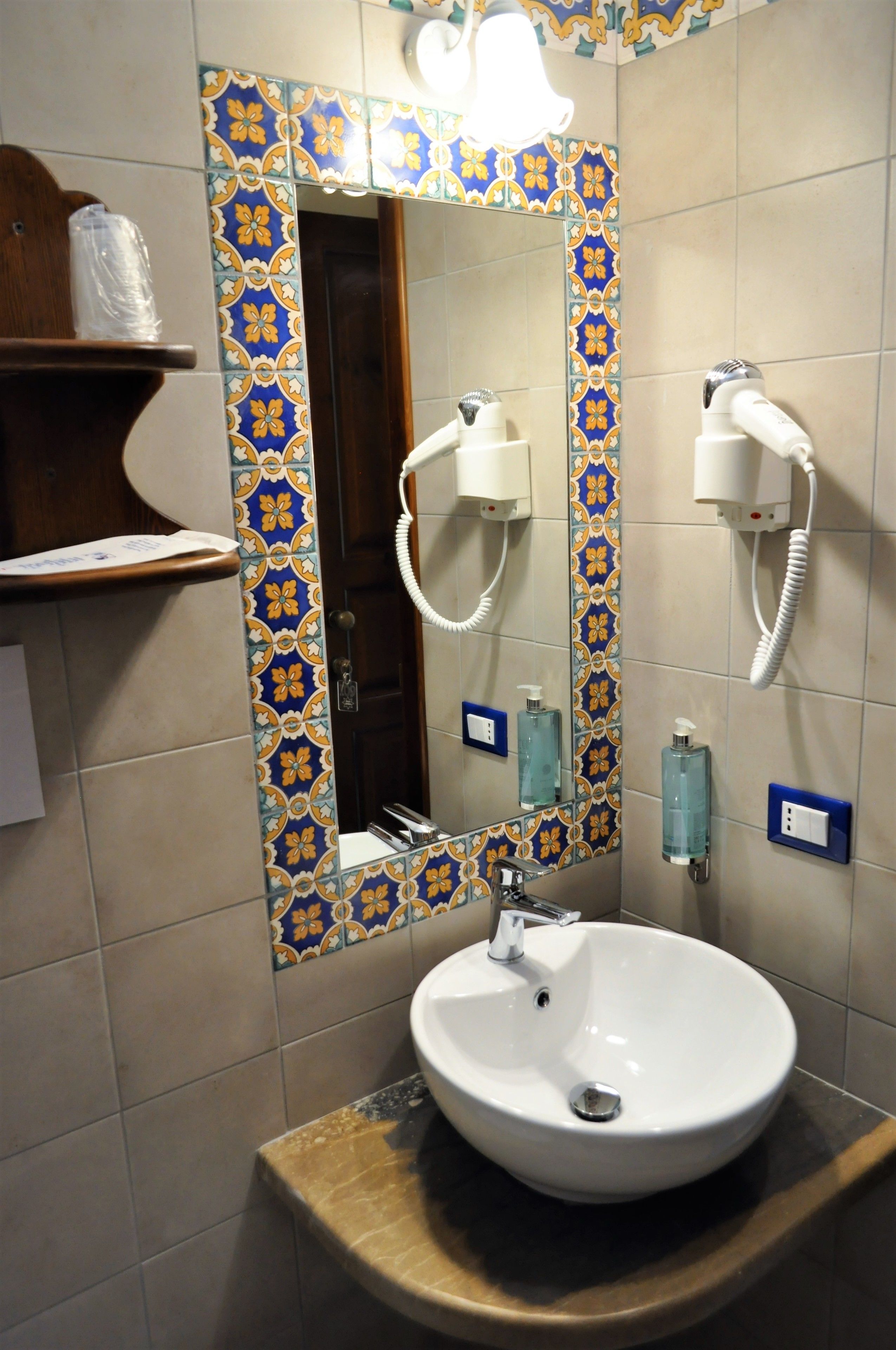 Un baño con un lavamanos blanco, un espejo con un borde de azulejos decorativos y un secador de pelo montado en la pared.