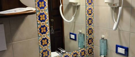 Un baño con un lavamanos blanco, un espejo con un borde de azulejos decorativos y un secador de pelo montado en la pared.