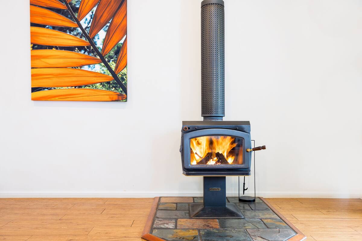 A wood-burning stove with a fire, a stone hearth, and a painting of leaves on the wall.