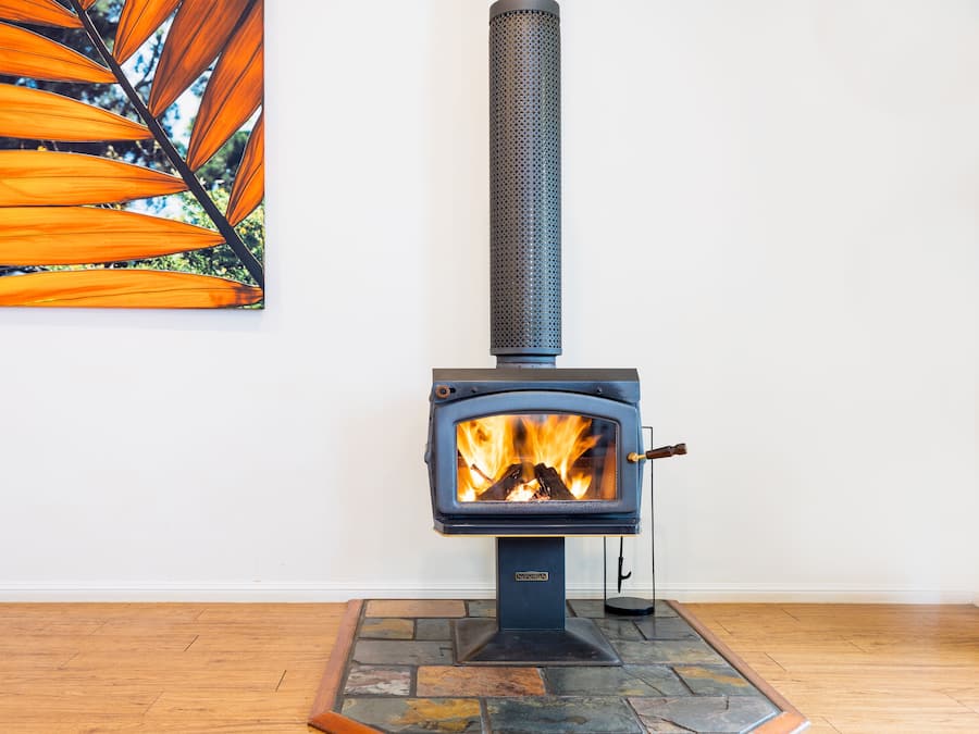 A wood-burning stove with a fire, a stone hearth, and a painting of leaves on the wall.