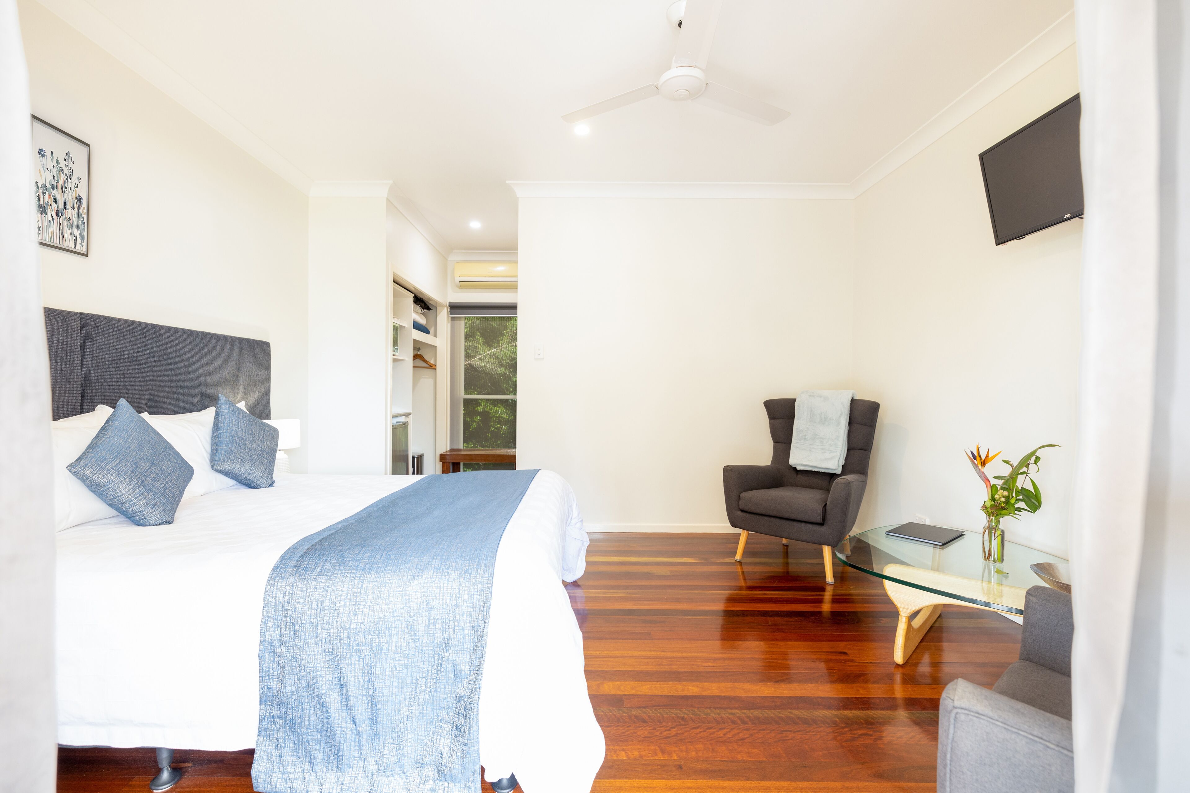 A modern bedroom with a bed, a chair, a glass table, and a TV.