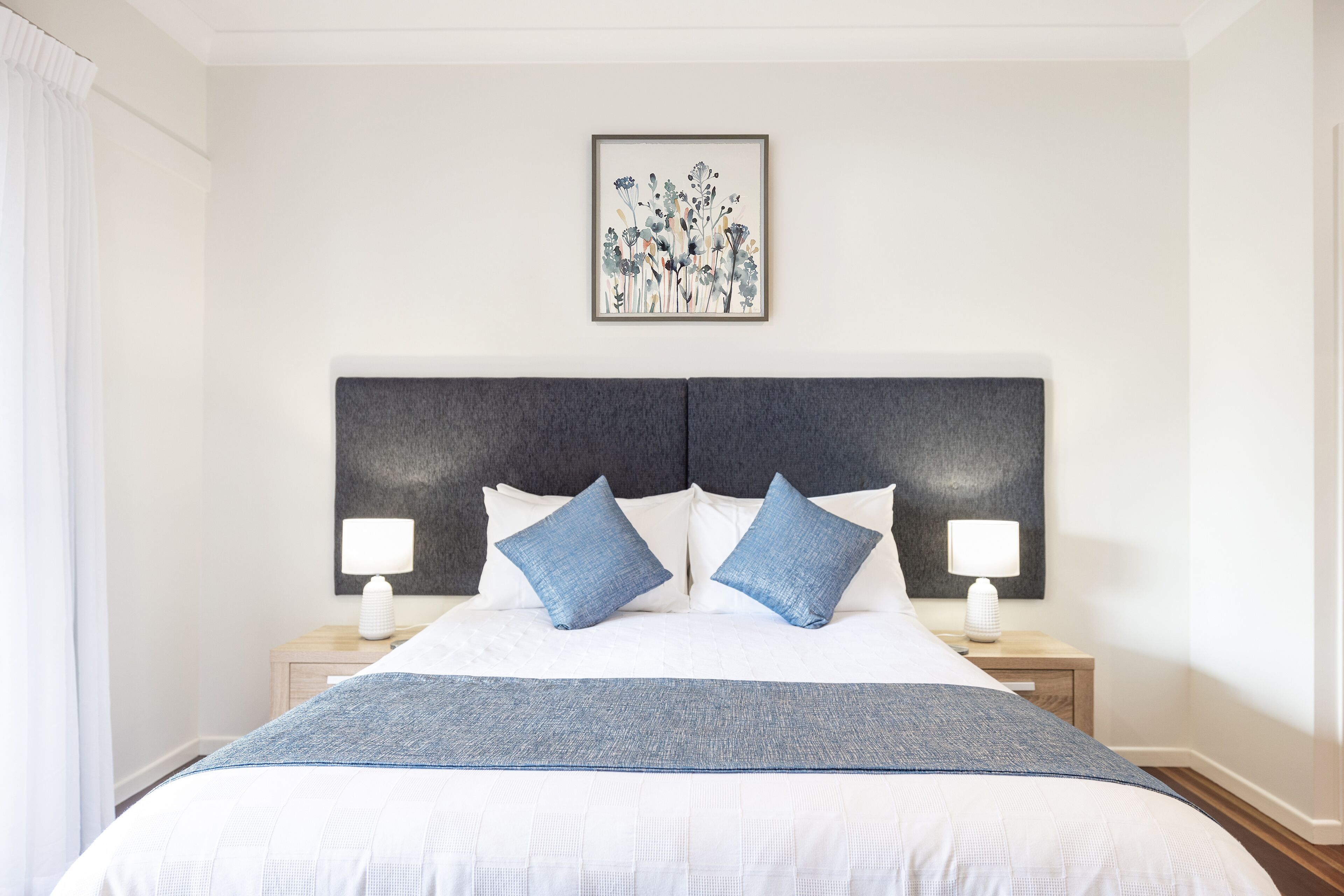 A neatly arranged bedroom with a large bed, two bedside tables with lamps, and a framed artwork on the wall.