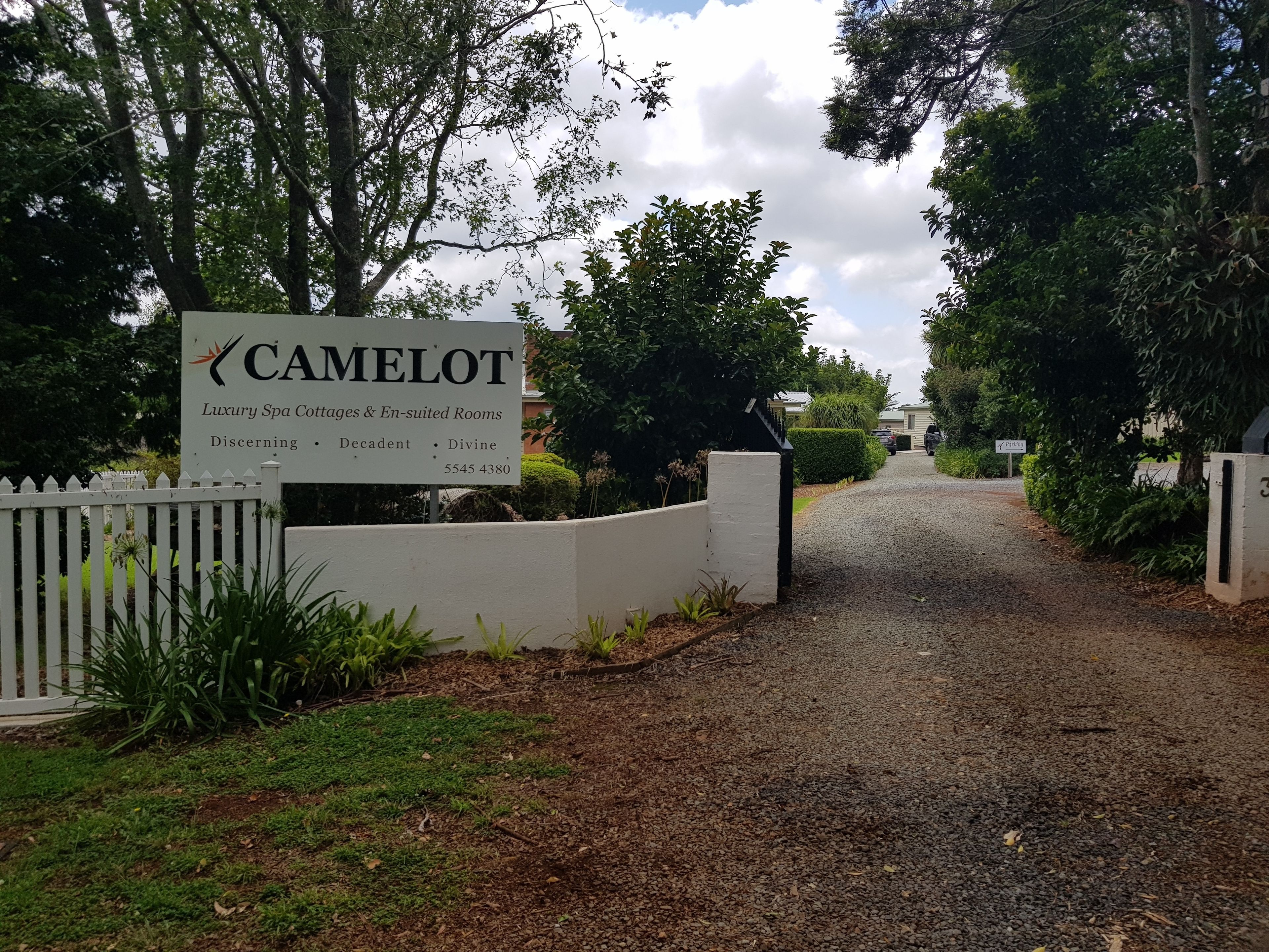 A sign for Camelot Luxury Spa Cottages & En-suited Rooms with a gravel driveway leading to the entrance.