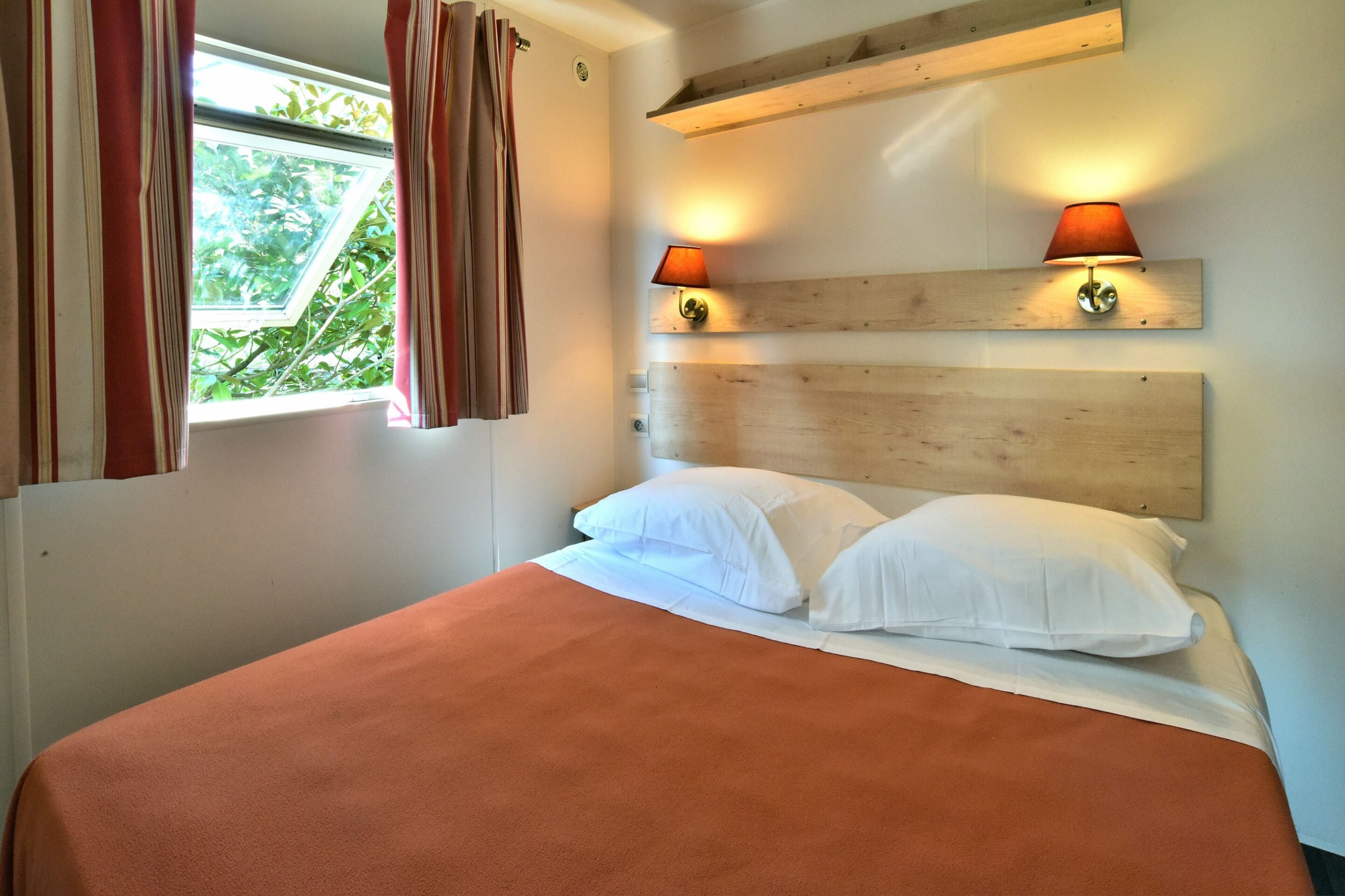 A bed with white linens, a wooden headboard, and two wall-mounted lamps.