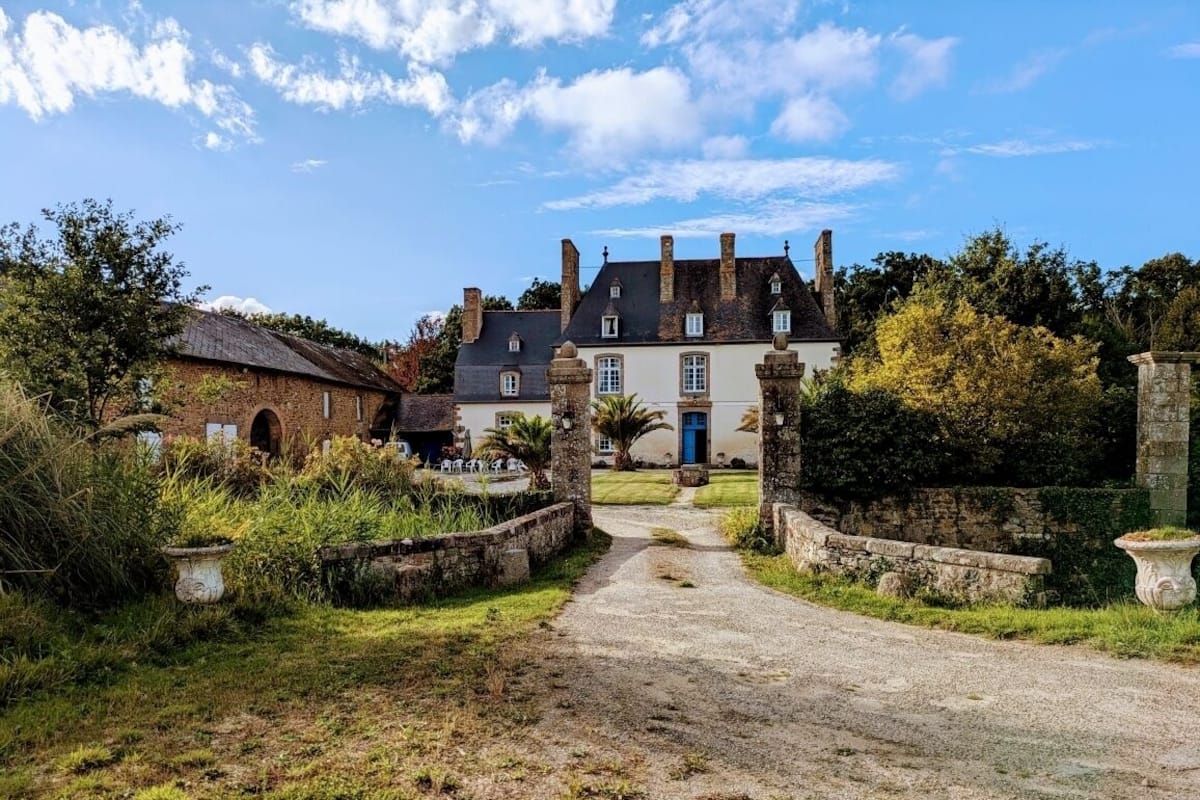 Un bâtiment historique, avec un chemin pavé menant à une porte bleue, entouré de verdure et de murs en pierre.