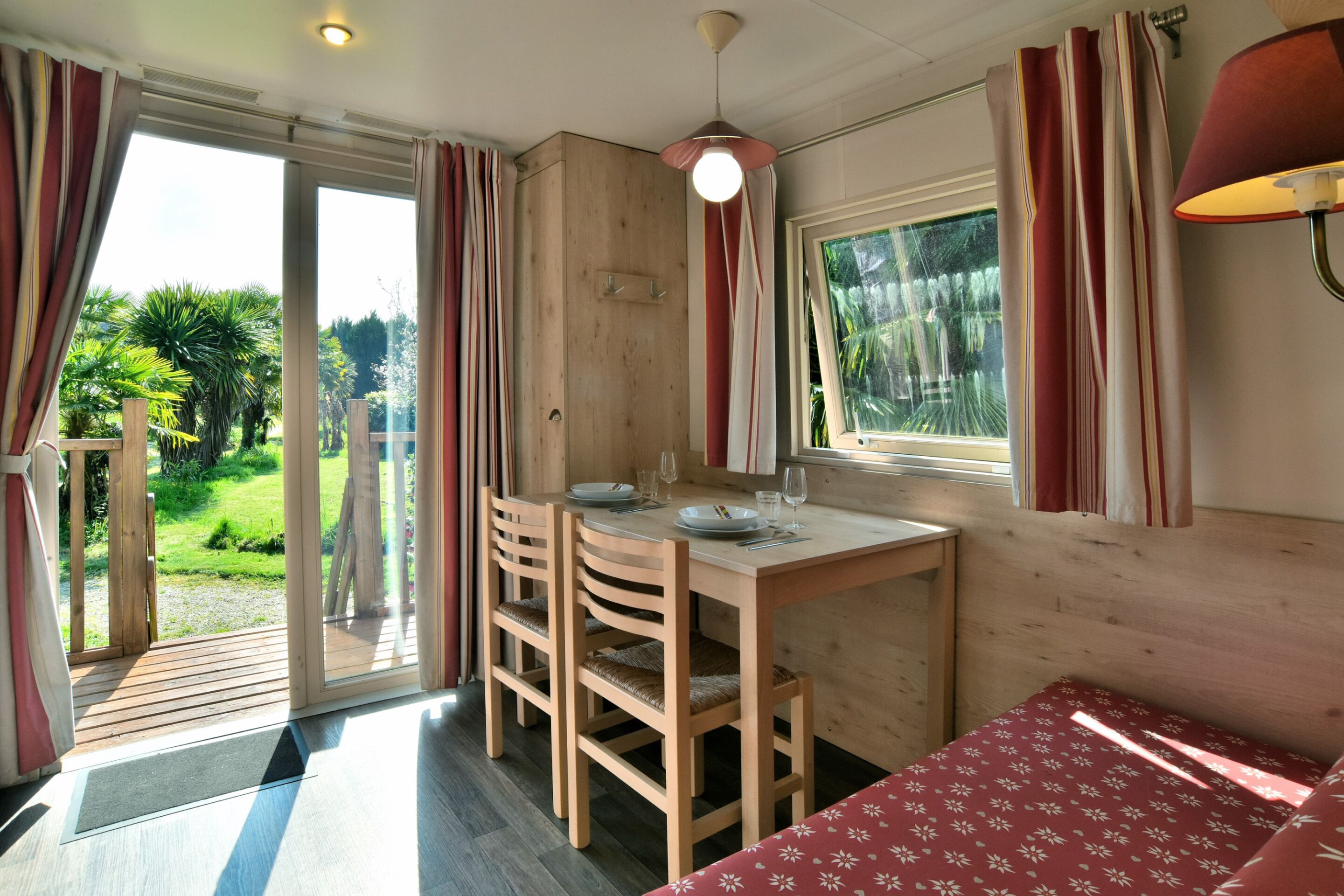 A room with a wooden table and chairs, a bed with a floral bedspread, and a window with curtains.