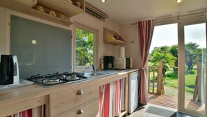 Una cocina con estufa a gas, microondas y cafetera. Hay muebles de madera y una ventana con vistas al verdor.