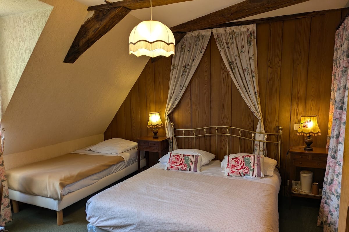 Une chambre avec deux lits simples, des murs en bois, un plafond en pente et deux lampes de chevet.