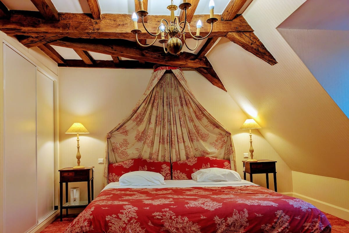 Une chambre à coucher avec un lit à baldaquin, des poutres en bois et deux lampes de chevet.