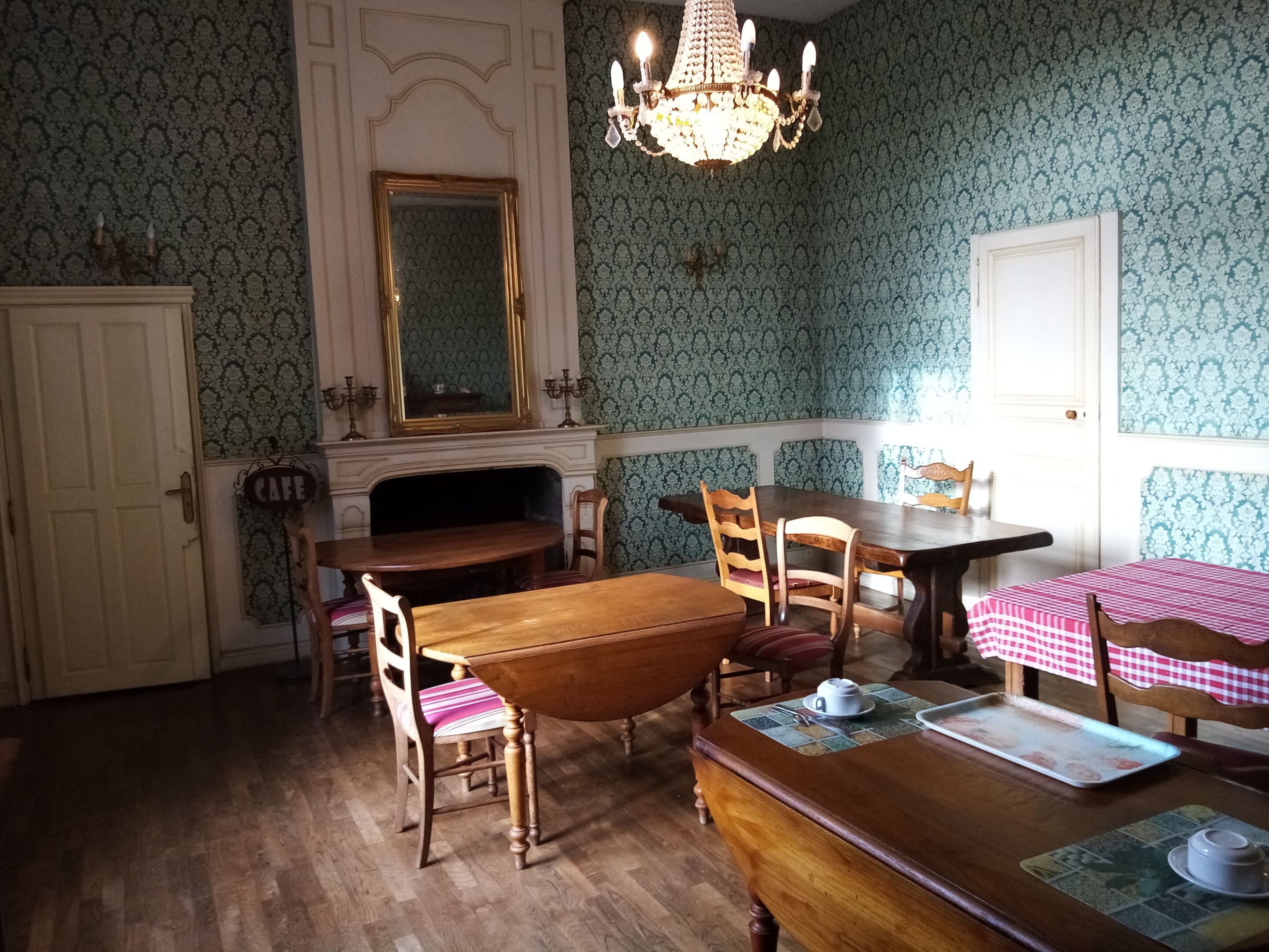 A dining area with wooden tables and chairs, a chandelier, and patterned wallpaper.