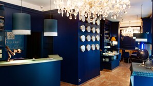 Een hotel lobby met een blauw kleurenschema, een kroonluchter, een receptiebalie en een muur met klokken.