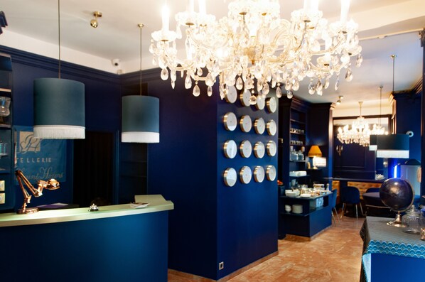 A hotel lobby with a blue color scheme, a chandelier, a reception desk, and a wall with clocks. - Hotel Petit Saint Honoré (Paris)