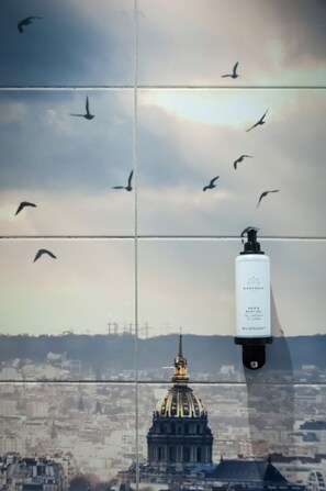 A bathroom with a tiled wall featuring a cityscape and a bottle of hair and body gel. - Hotel Petit Saint Honoré (Paris)