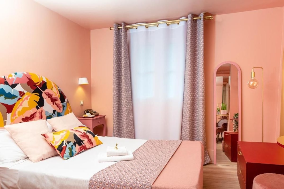 A bedroom with a bed, pillows, a bedside table, a lamp, a mirror, and a wardrobe.