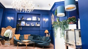 Een kamer met een blauwe wand, een donkergroene bank, een kroonluchter en een blauwe hanglamp.