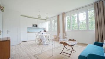 Una cocina moderna con armarios blancos, un comedor con mesa y sillas, y vistas a través de amplios ventanales.