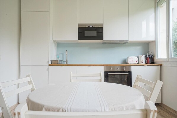 A compact kitchen with white cabinets, a microwave, an oven, and a coffee maker on the countertop. - Hotel Petit Saint Honoré (Paris)