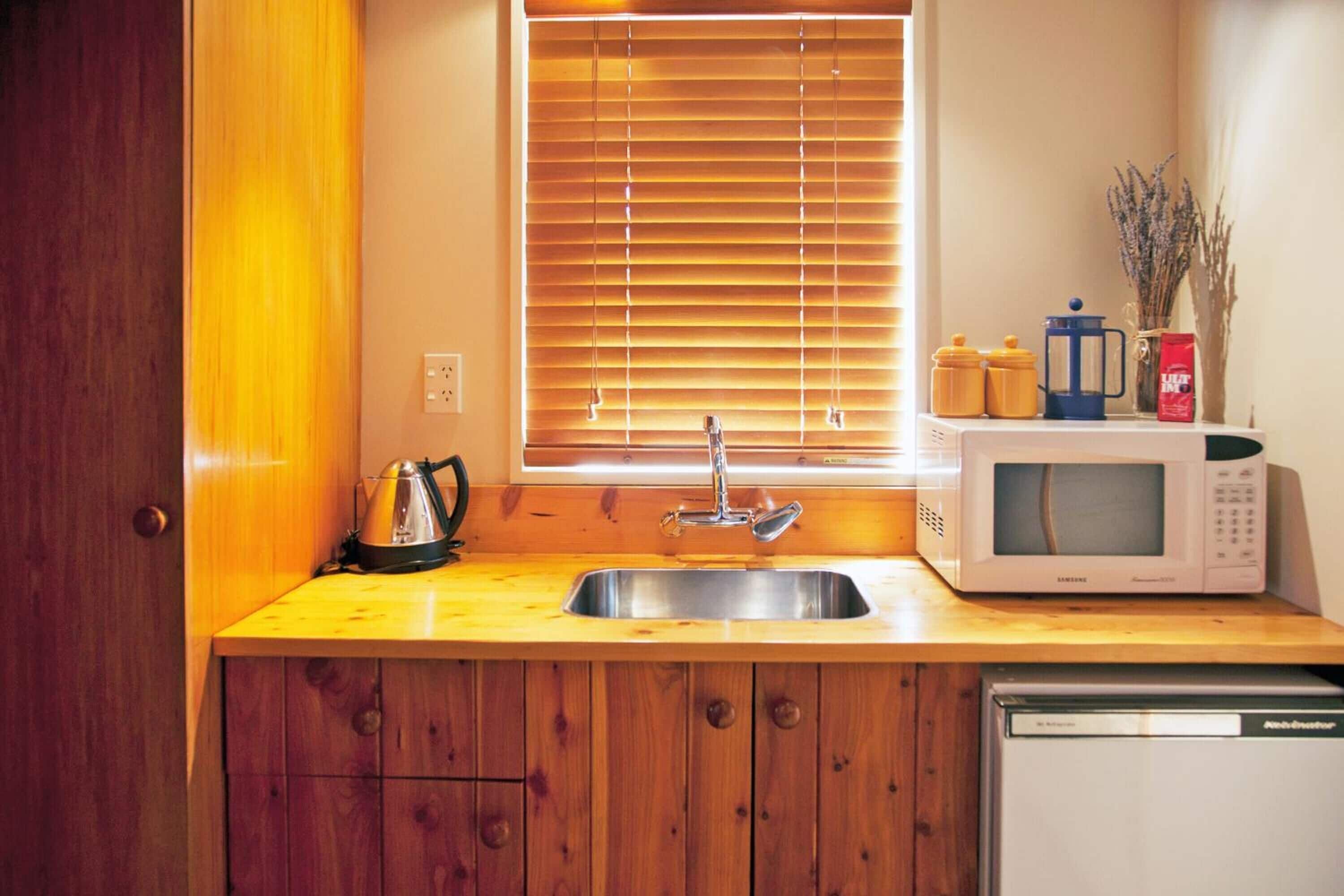Een compacte keuken met een houten aanrecht, een roestvrijstalen spoelbak, een magnetron en een koffiezetapparaat.