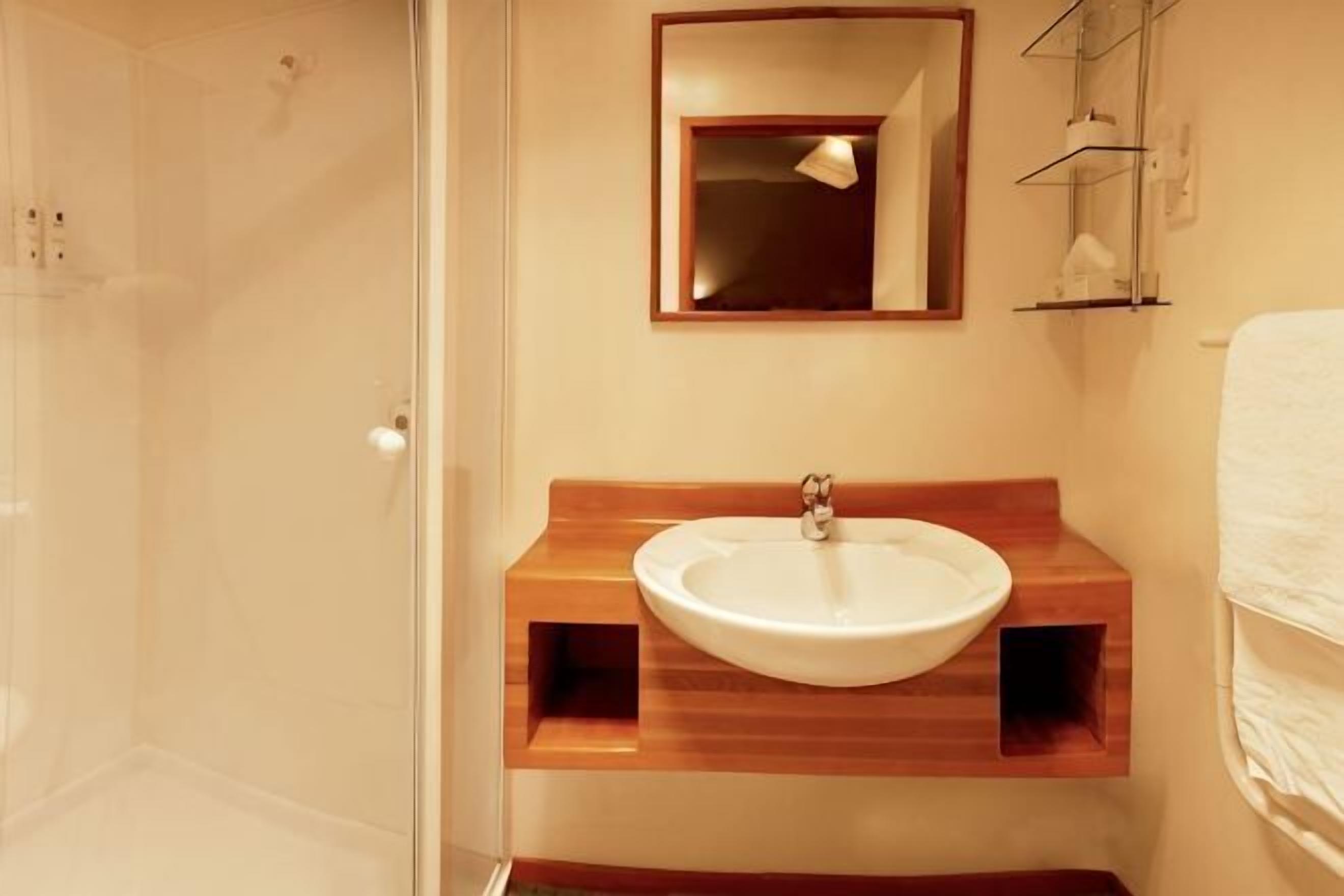 Un bagno con un mobile bagno in legno, un lavello, uno specchio e un box doccia in vetro.