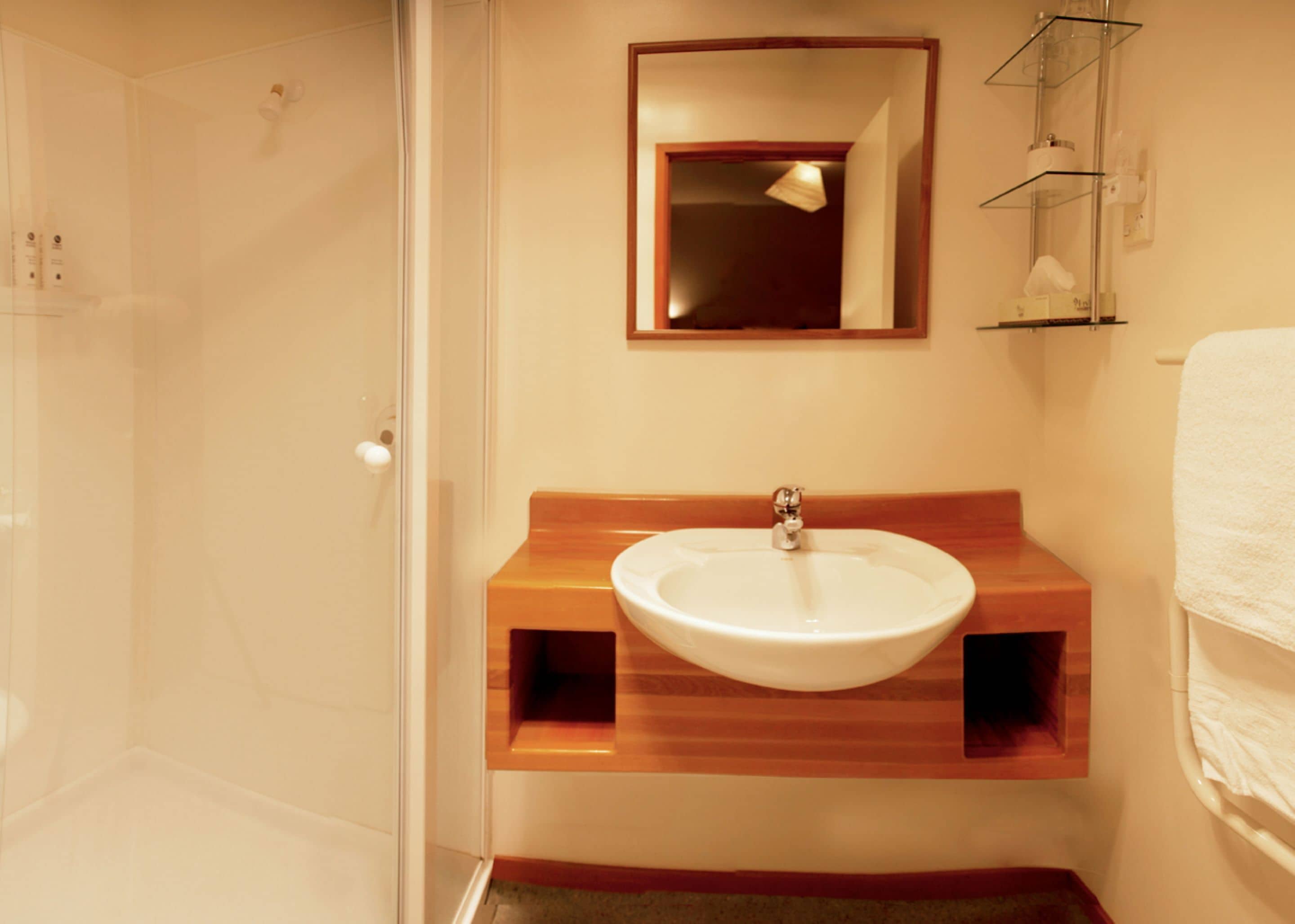 Een badkamer met een wit wastafel, houten opbergmeubel en een spiegel erboven.