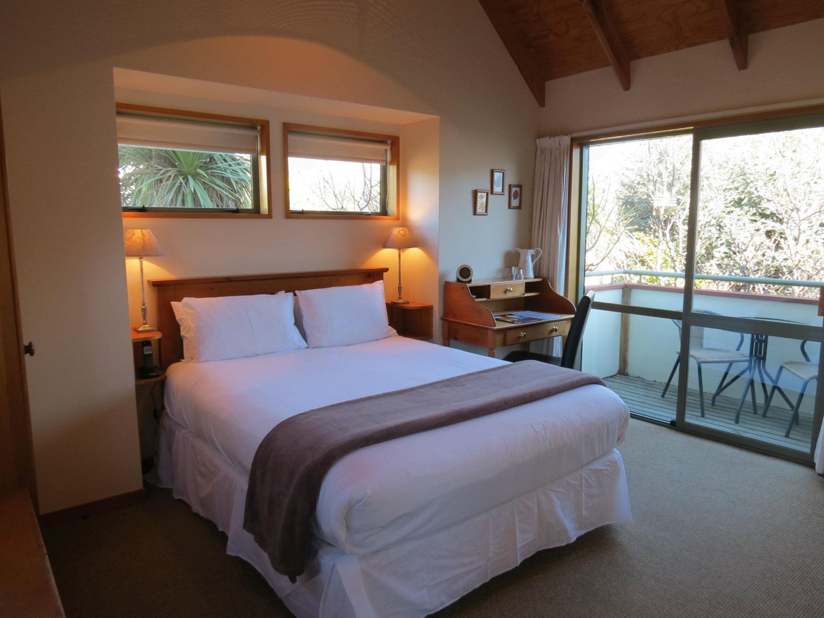 A hotel room with a large bed, a desk, and a balcony with chairs.