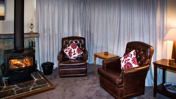 Un salon chaleureux avec une cheminée, deux fauteuils en cuir ornés de coussins à motifs floraux, une petite table en bois et une lampe.