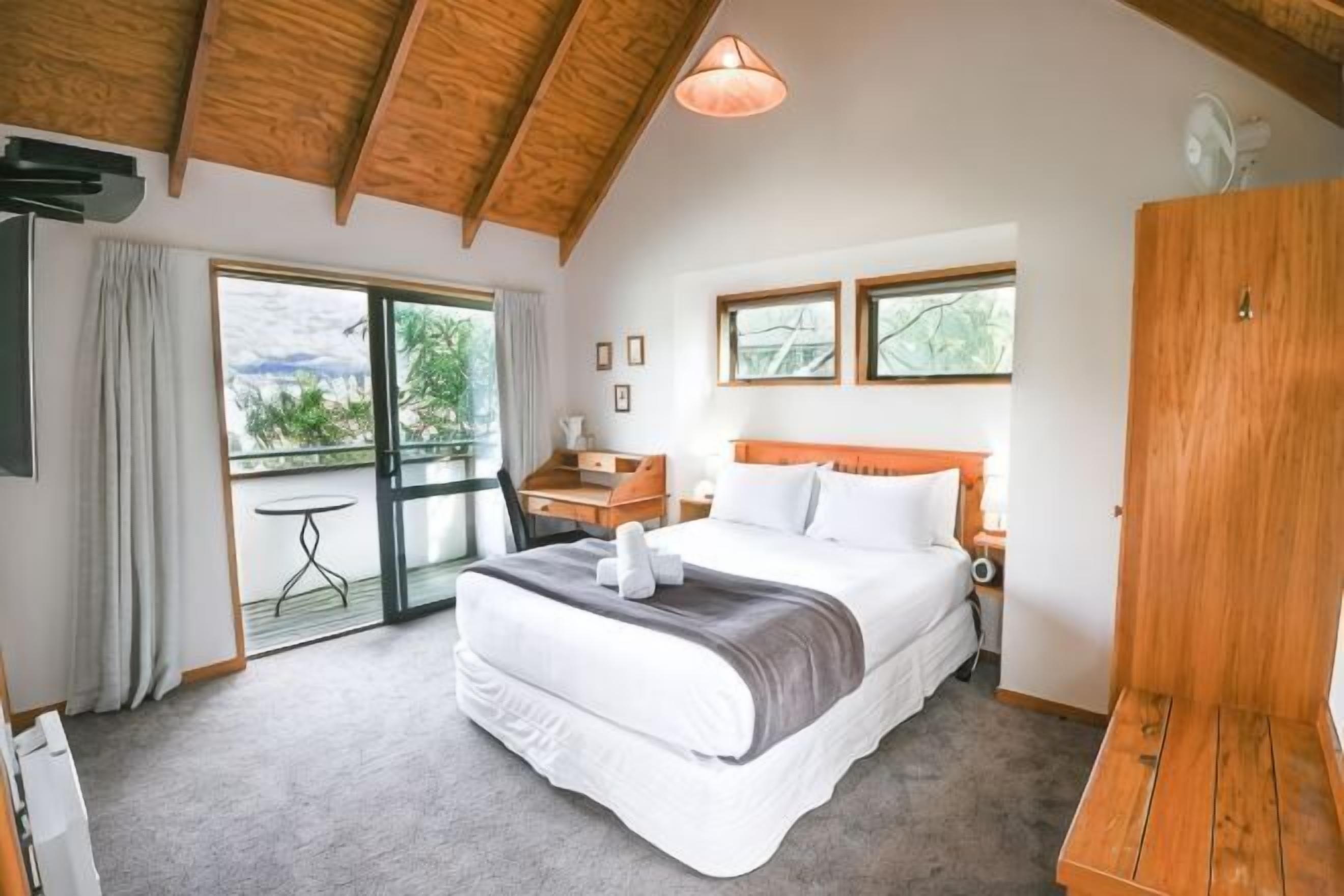 Una camera da letto con un letto, un armadio in legno, una scrivania e un balcone con vista.
