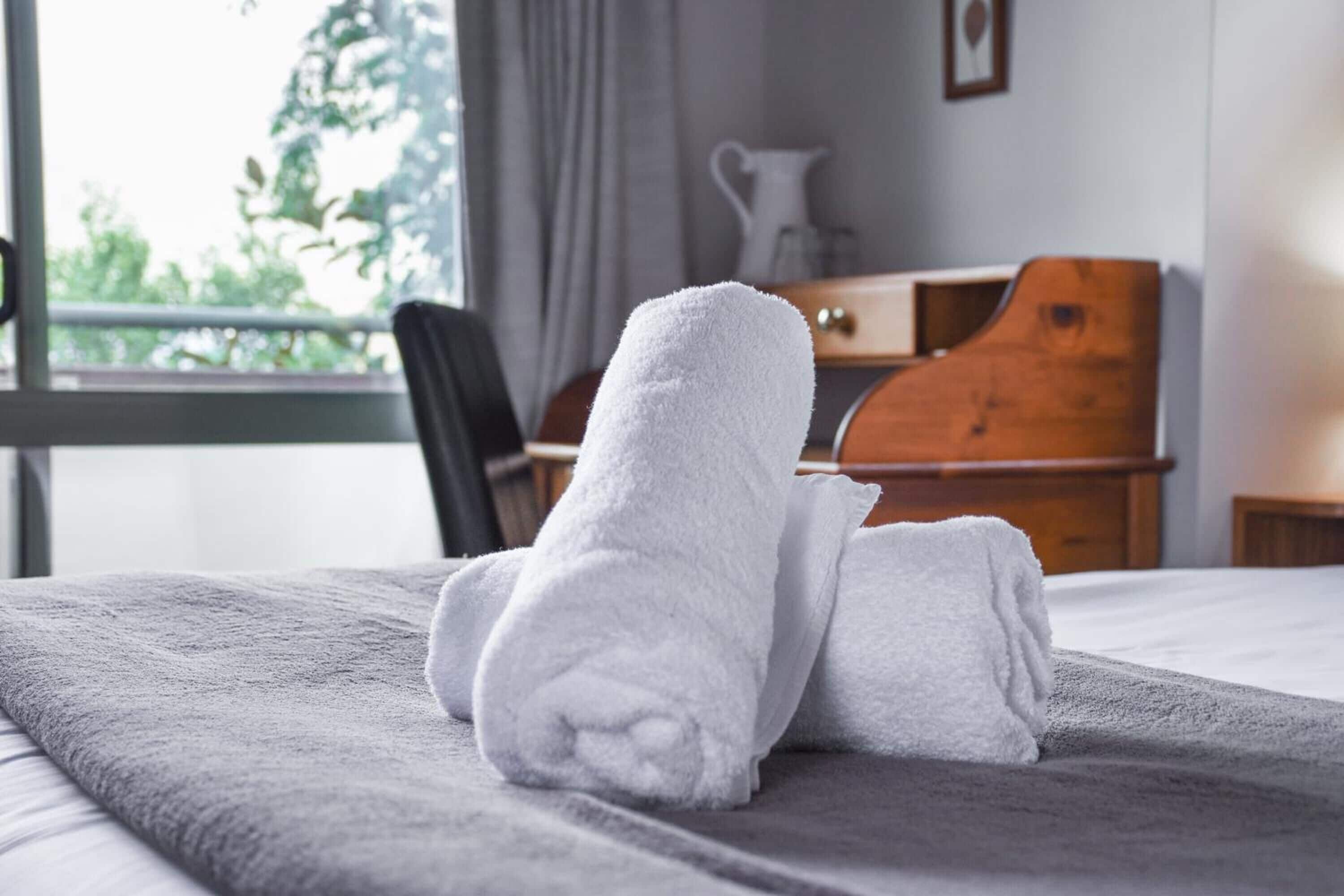 A neatly made bed with a gray blanket and two white towels folded on top.