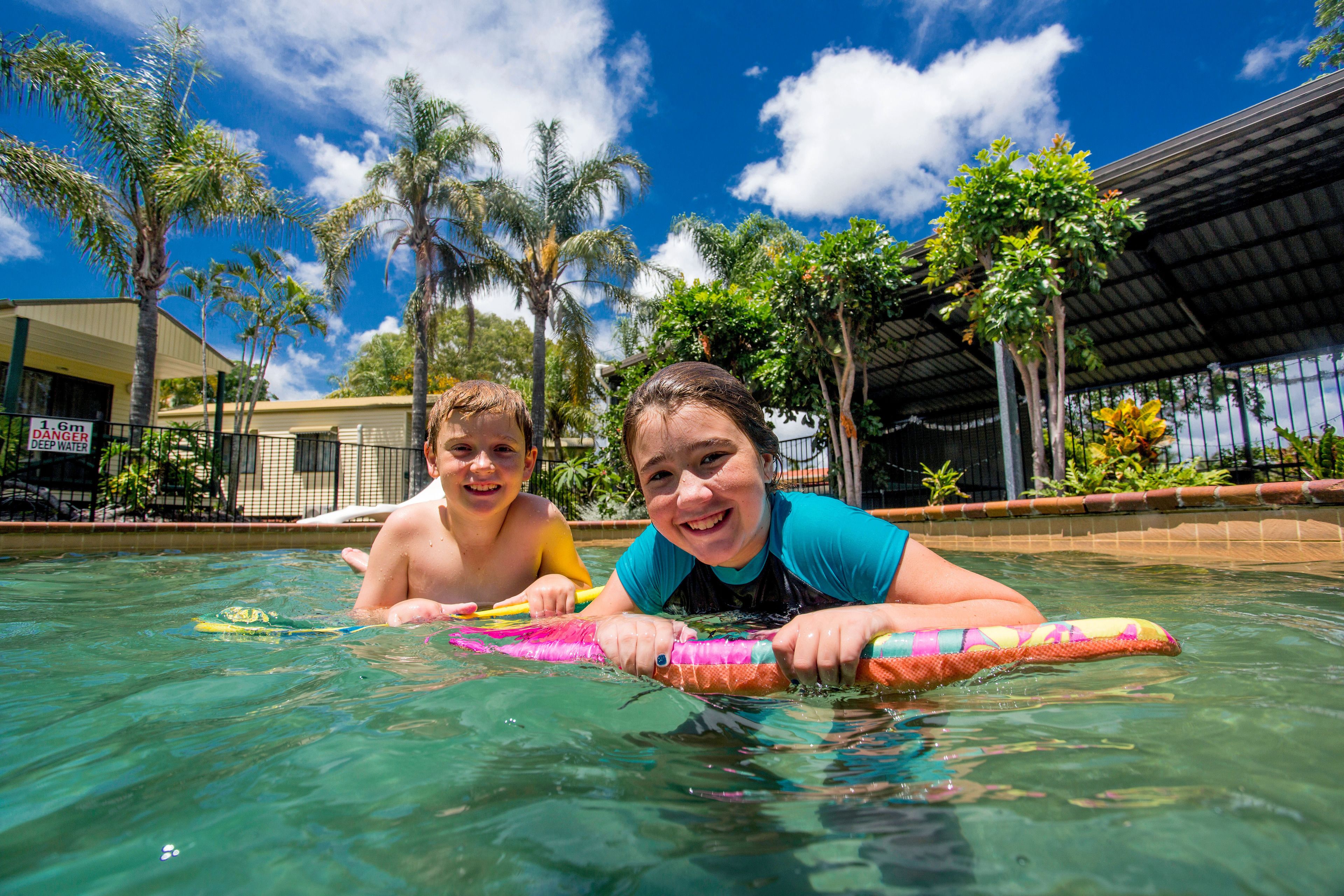 Two people in a swimming pool with palm trees and a building in the background.