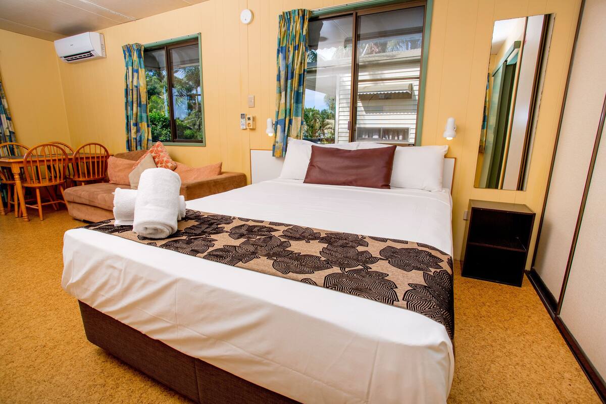 Una habitación de hotel con cama, sofá, mesa de comedor con sillas y ventana con cortinas.