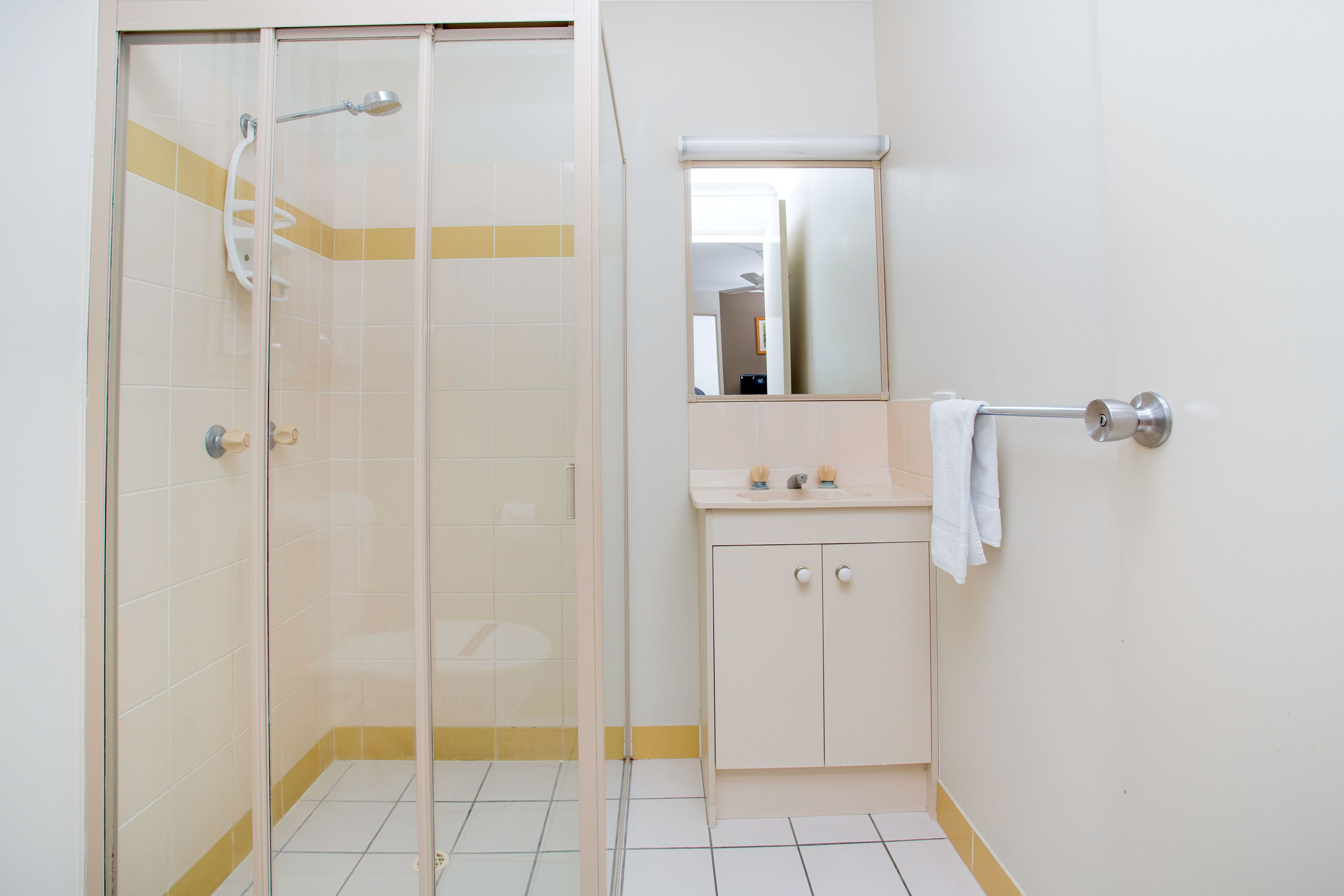 A bathroom with a glass-enclosed shower, a white sink with a mirror above it, and a towel hanging on the wall.