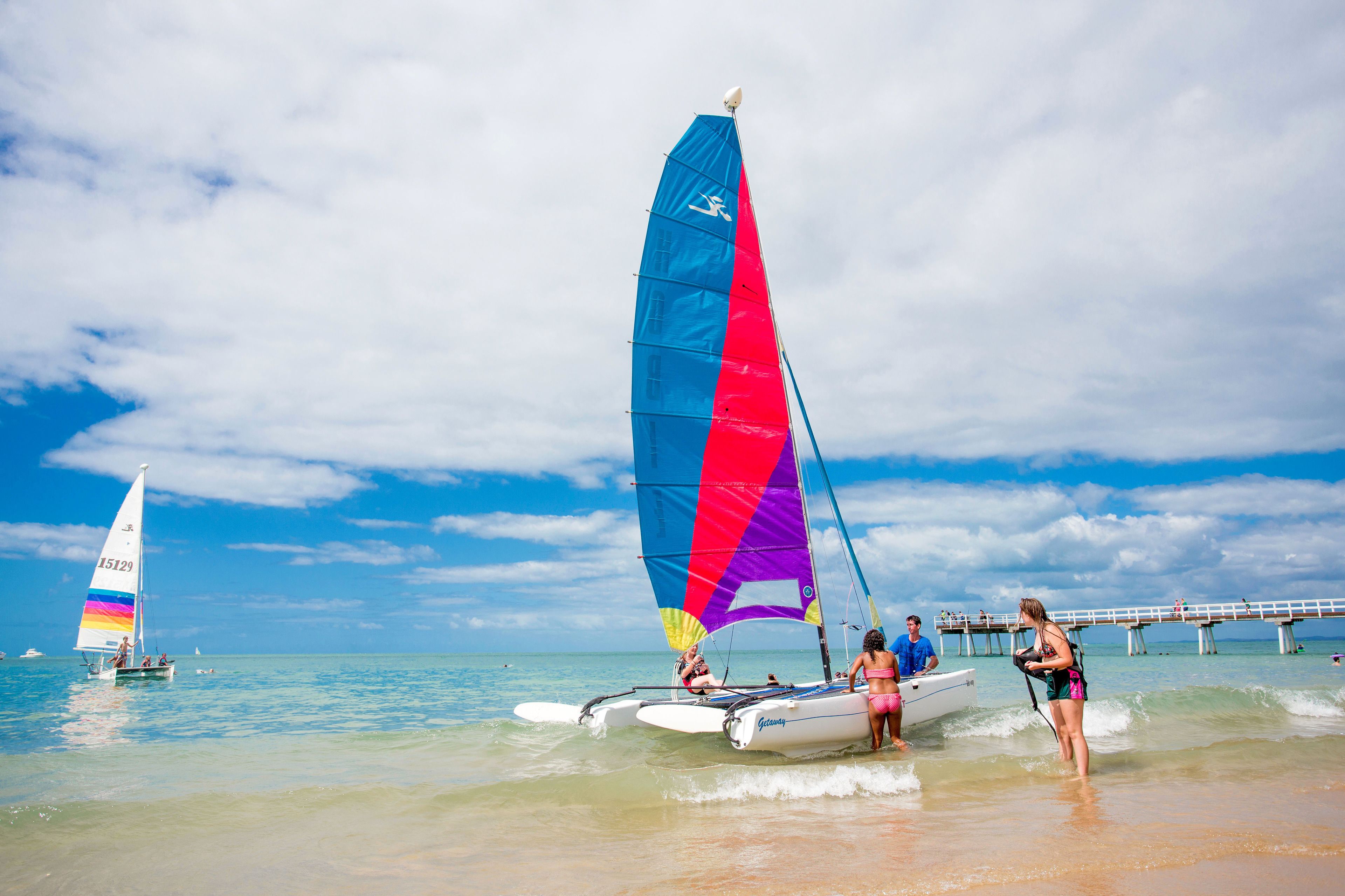A beach scene with a sailboat and a jet ski.