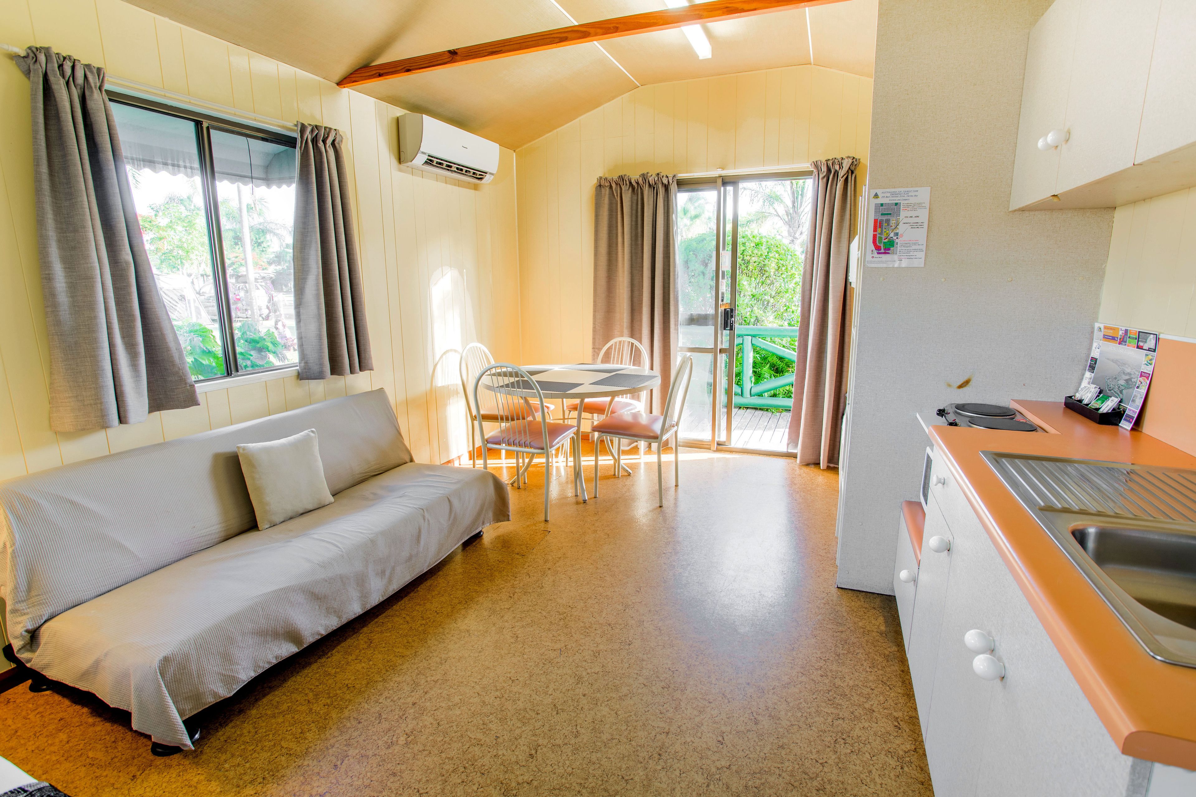 A cozy room with a sofa, a dining table with chairs, a kitchenette, and a sliding glass door leading to an outdoor area.