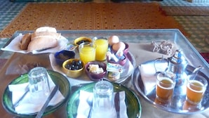 Une table de petit-déjeuner avec divers aliments et boissons, une assiette en verre vert, une théière en argent et un plateau avec deux verres de thé.