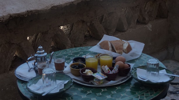 Une table dressée avec des aliments pour le petit-déjeuner, notamment du pain, des fruits et des boissons, donnant sur un paysage désertique.